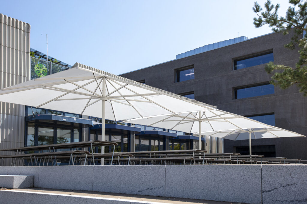 Home Large white commercial-grade architectural umbrellas providing high-wind rated shade for a modern hospitality patio.